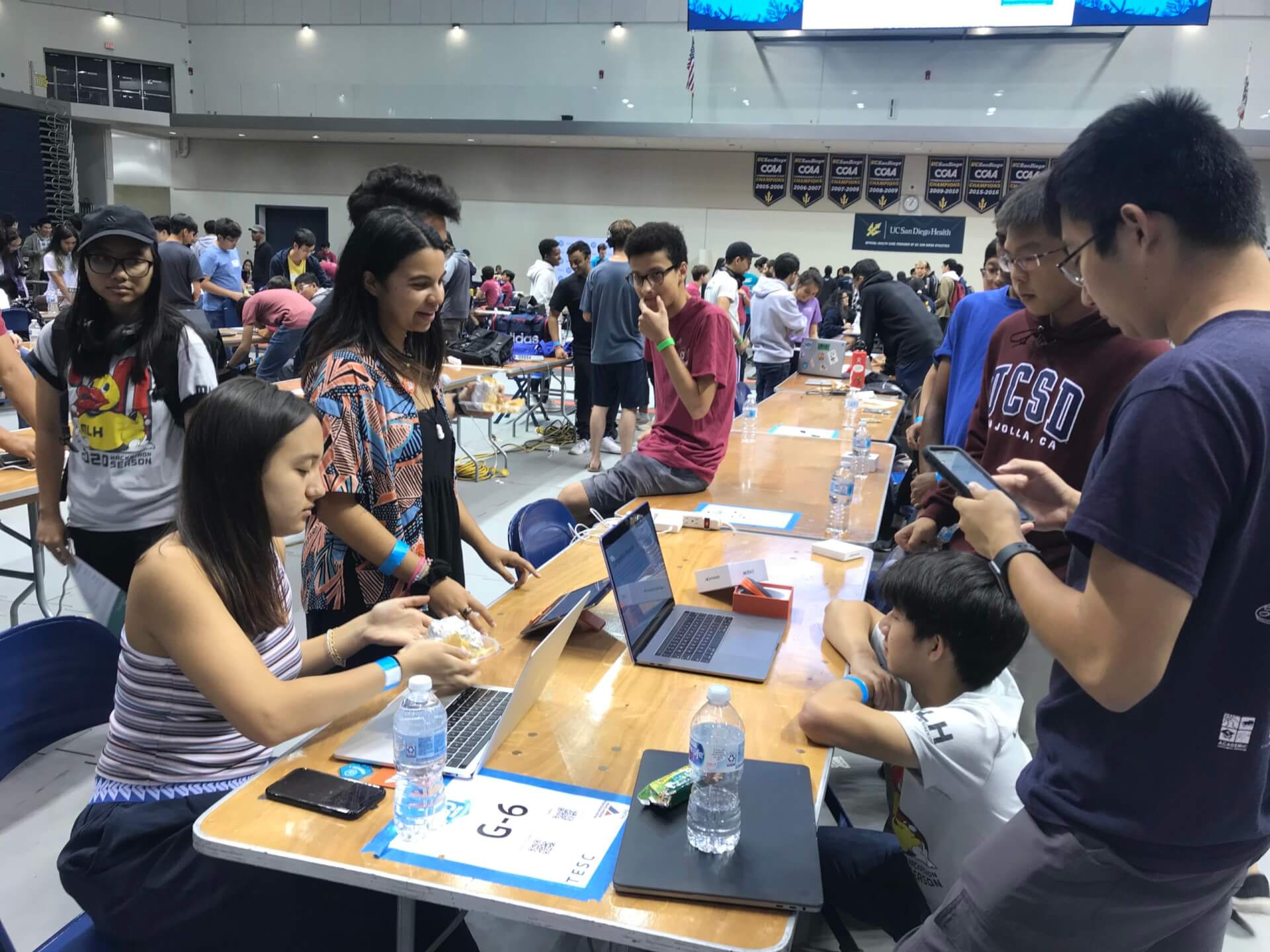 Crowded gymnasium filled with college-aged students at a hackathon.